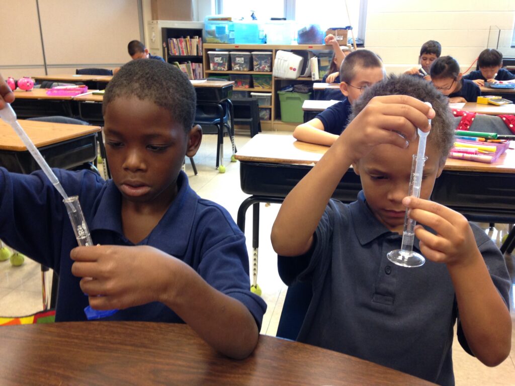 Two male students are using pipettes and graduated cylinders to measure liquids