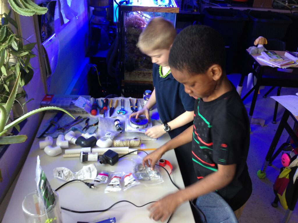 Two male students organize equipment and tools on a table in preparation for tank construction